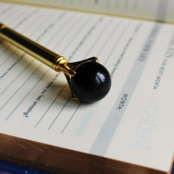 Black obsidian crystal pen for protection lying on open spiritual journal
