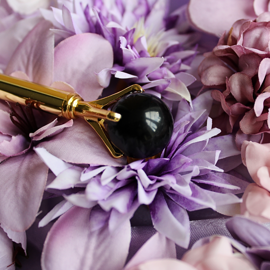 Black obsidian crystal pen lying on a bed of flowers