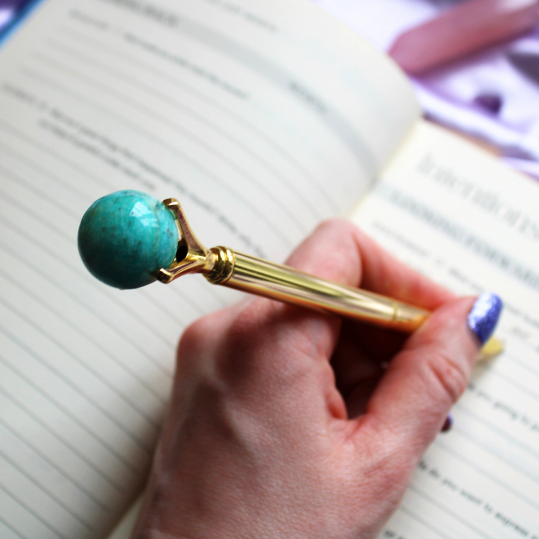 A person writing in a gratitude journal holding an Amazonite crystal ball pen