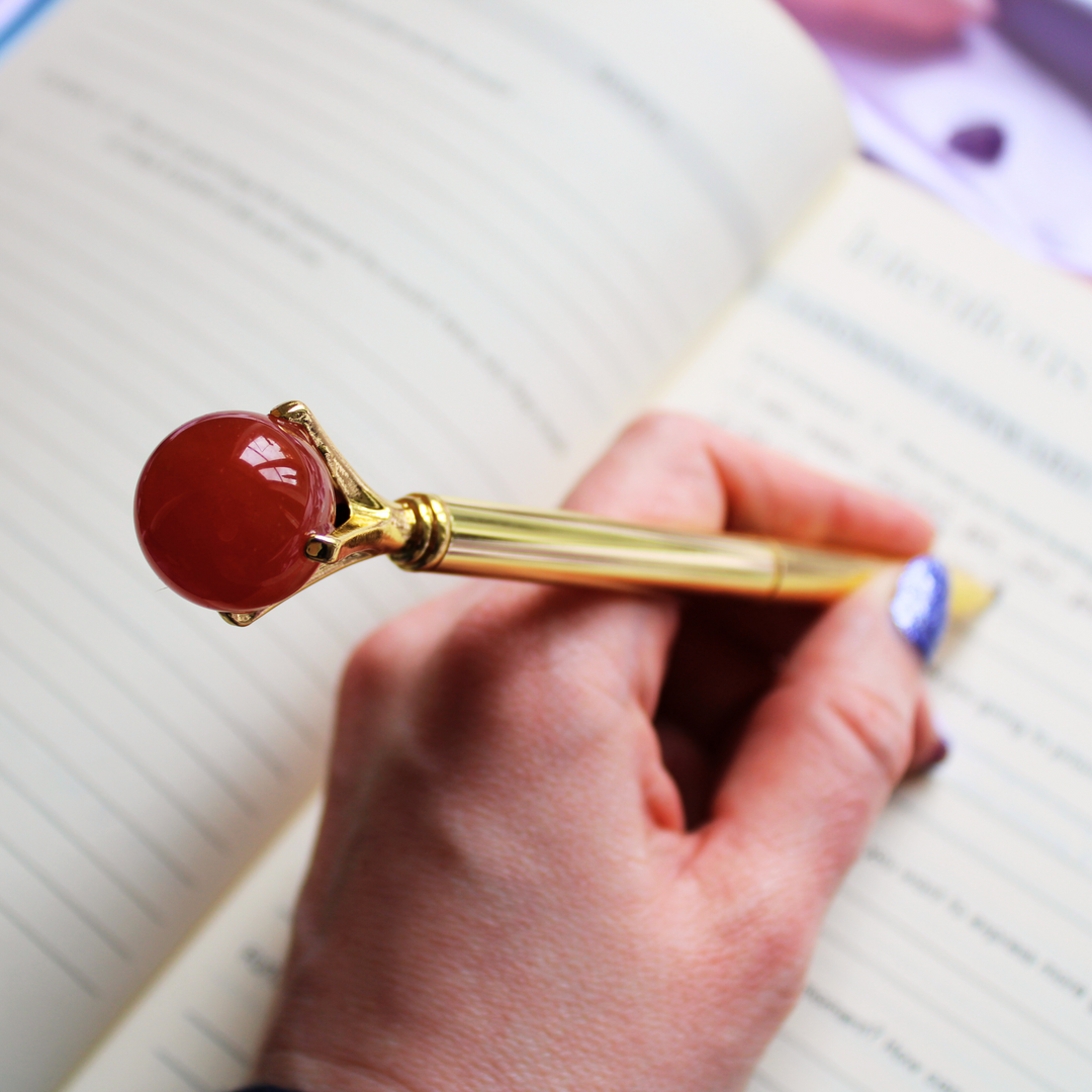 Writing in a guided gratitude journal holding a red Carnelian crystal ball pen