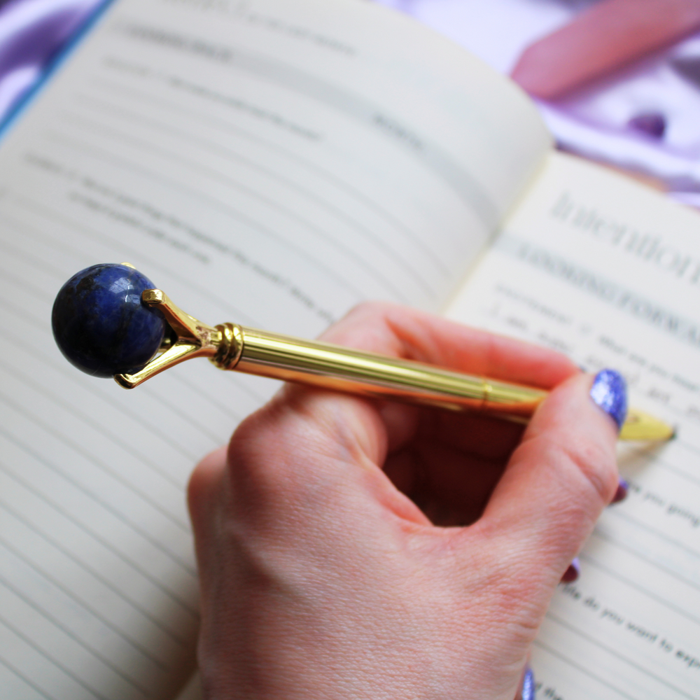 Hand writing in a gratitude journal holding a Sodalite crystal ball pen
