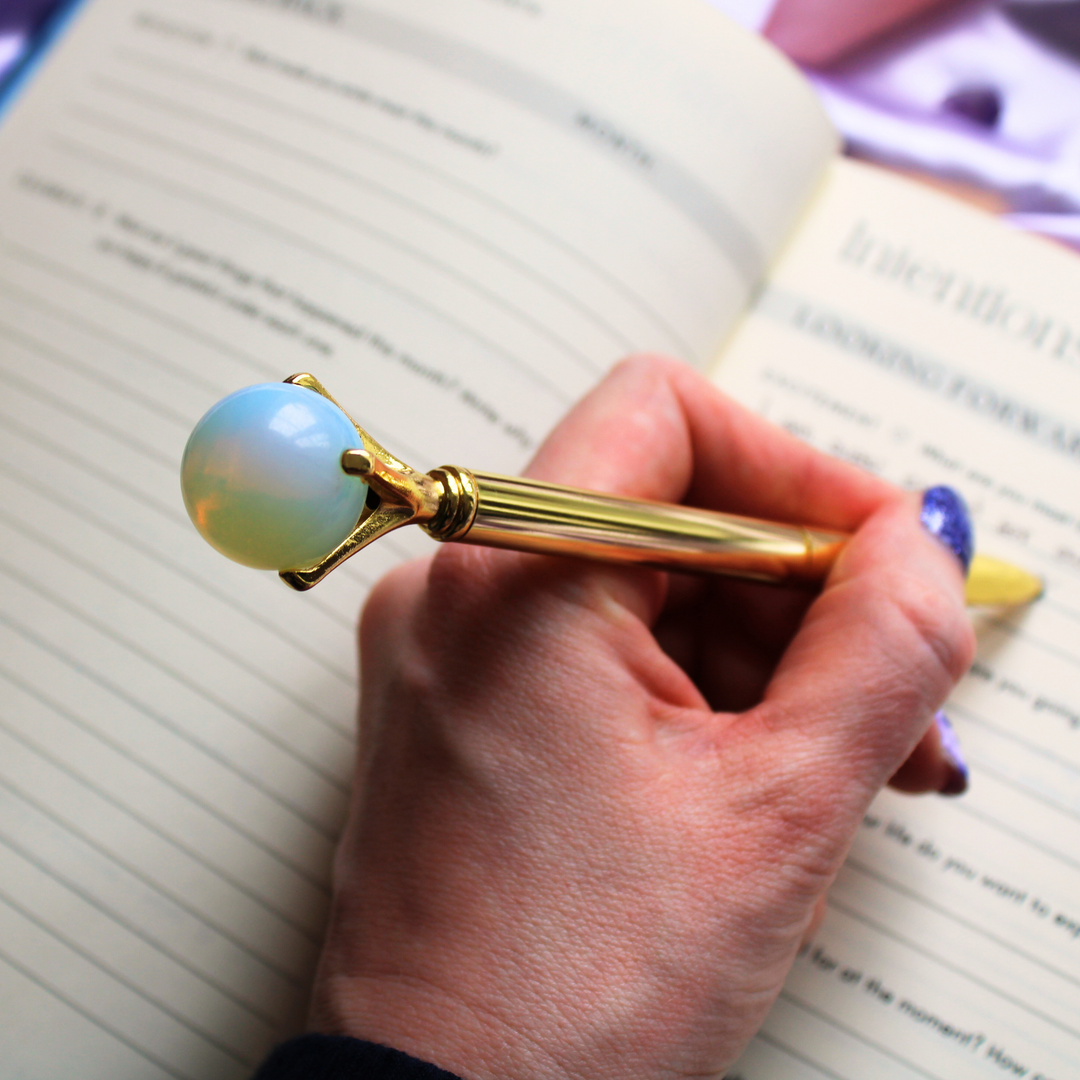 A person writing in a gratitude journal holding an Opal crystal ball pen