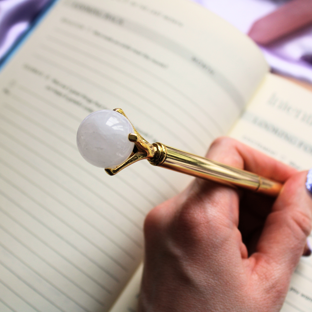 A person writing in a gratitude journal holding an Clear Quartz ball pen