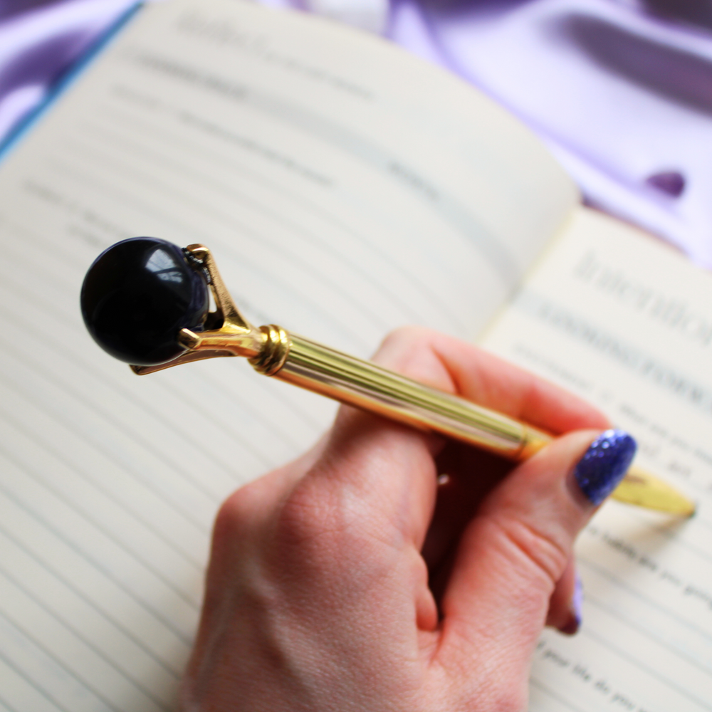Person writing in a gratitude journal holding a black obsidian crystal ball pen