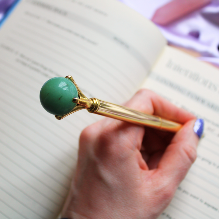 Writing in a gratitude journal holding a Green Aventurine crystal ball pen