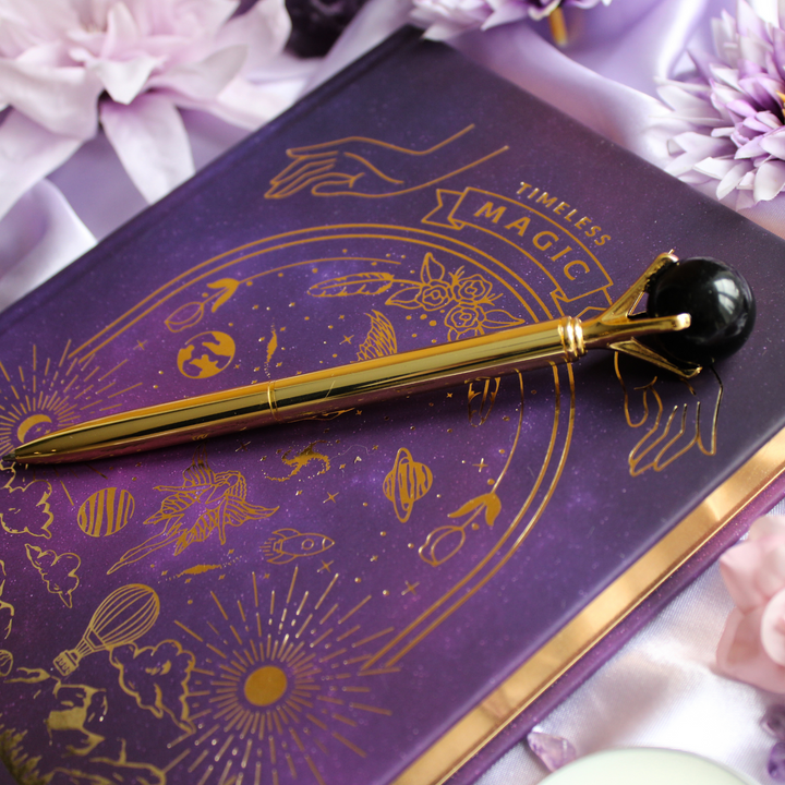 Protection crystal pen with black obsidian crystal ball on top of purple & gold manifestation journal