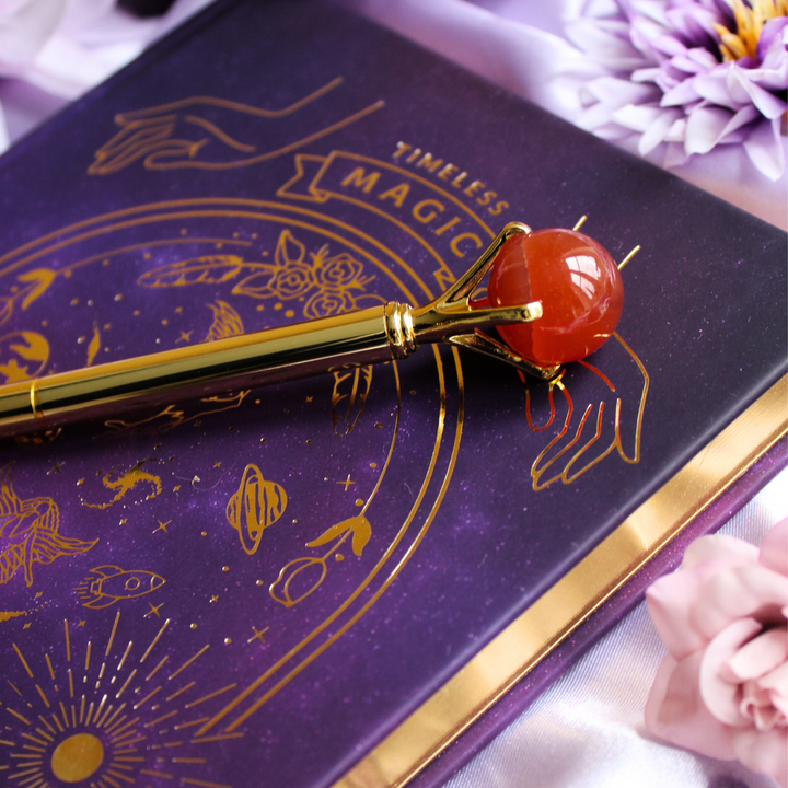 Carnelian pen on top of a gold manifestation journal