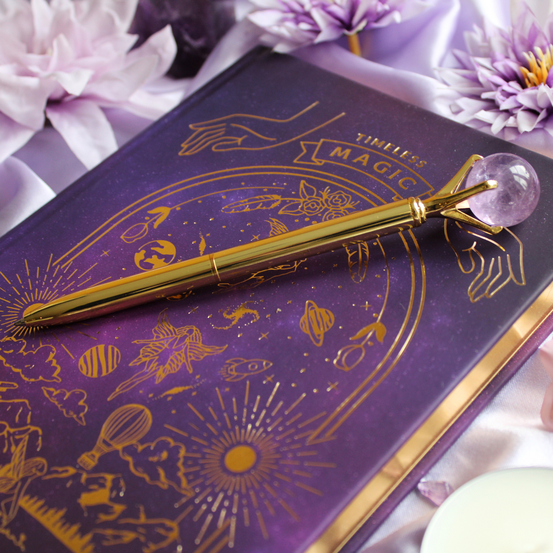 Amethyst crystal pen to reduce stress on top of a purple & gold manifestation journal