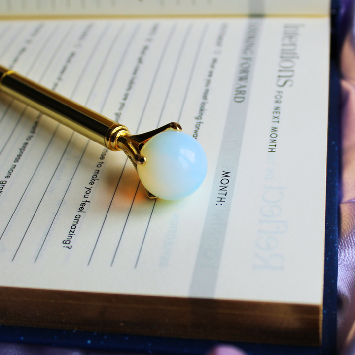 Opal crystal pen to balance emotions lying on an open daily gratitude journal