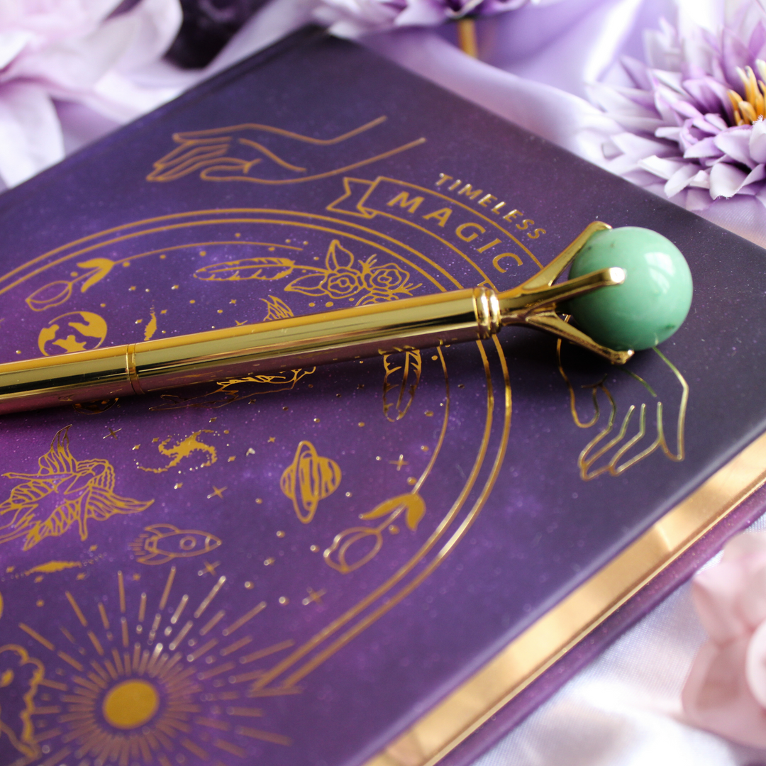 Green Aventurine crystal pen for good luck resting on a manifestation journal