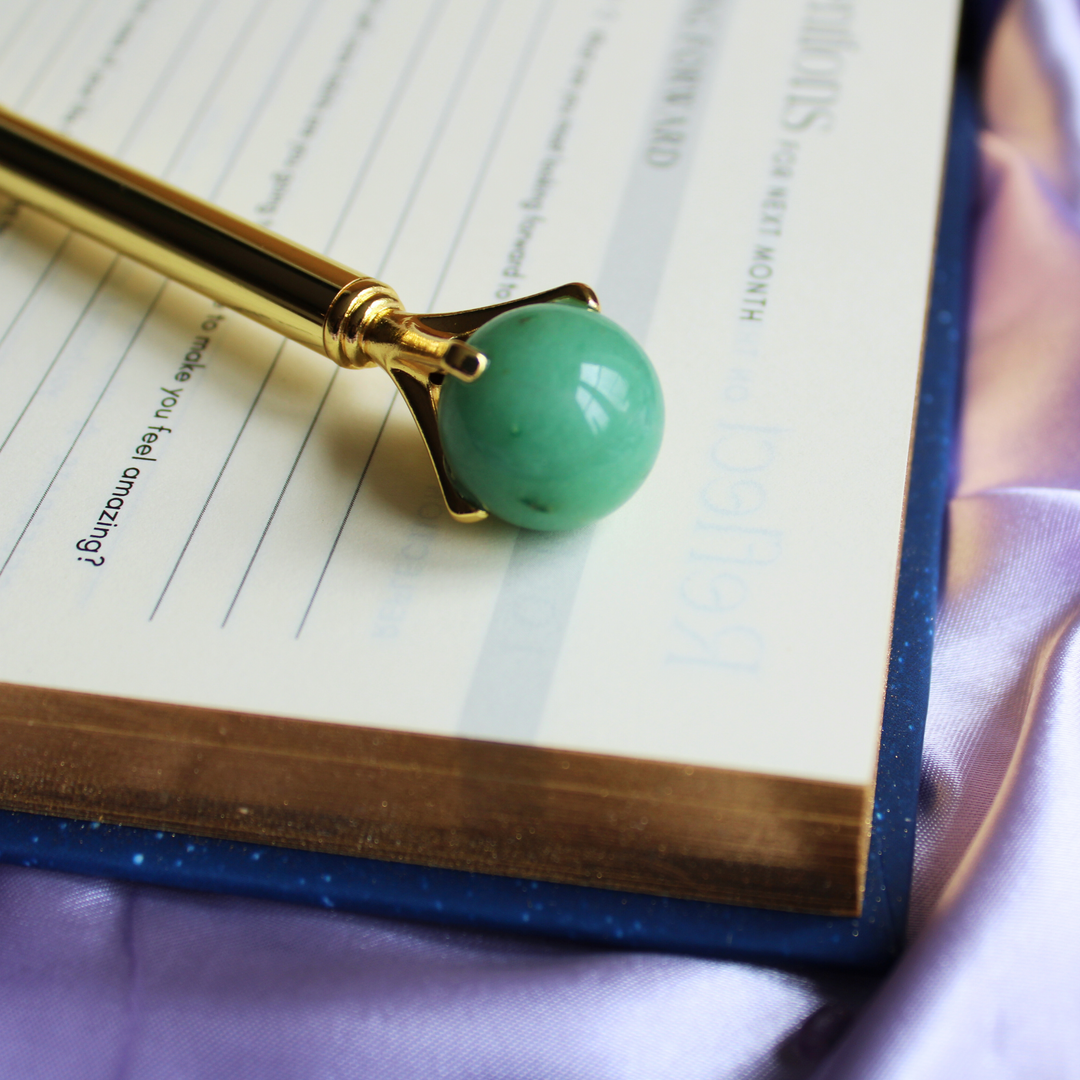 Green Aventurine crystal ball pen for bringing good luck on top of a celestial spiritual journal