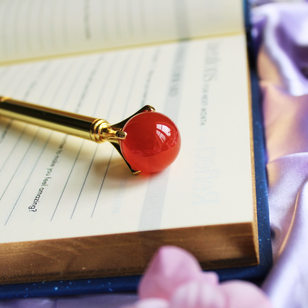 Carnelian crystal ball pen for increasing motivation on top of a spiritual journal