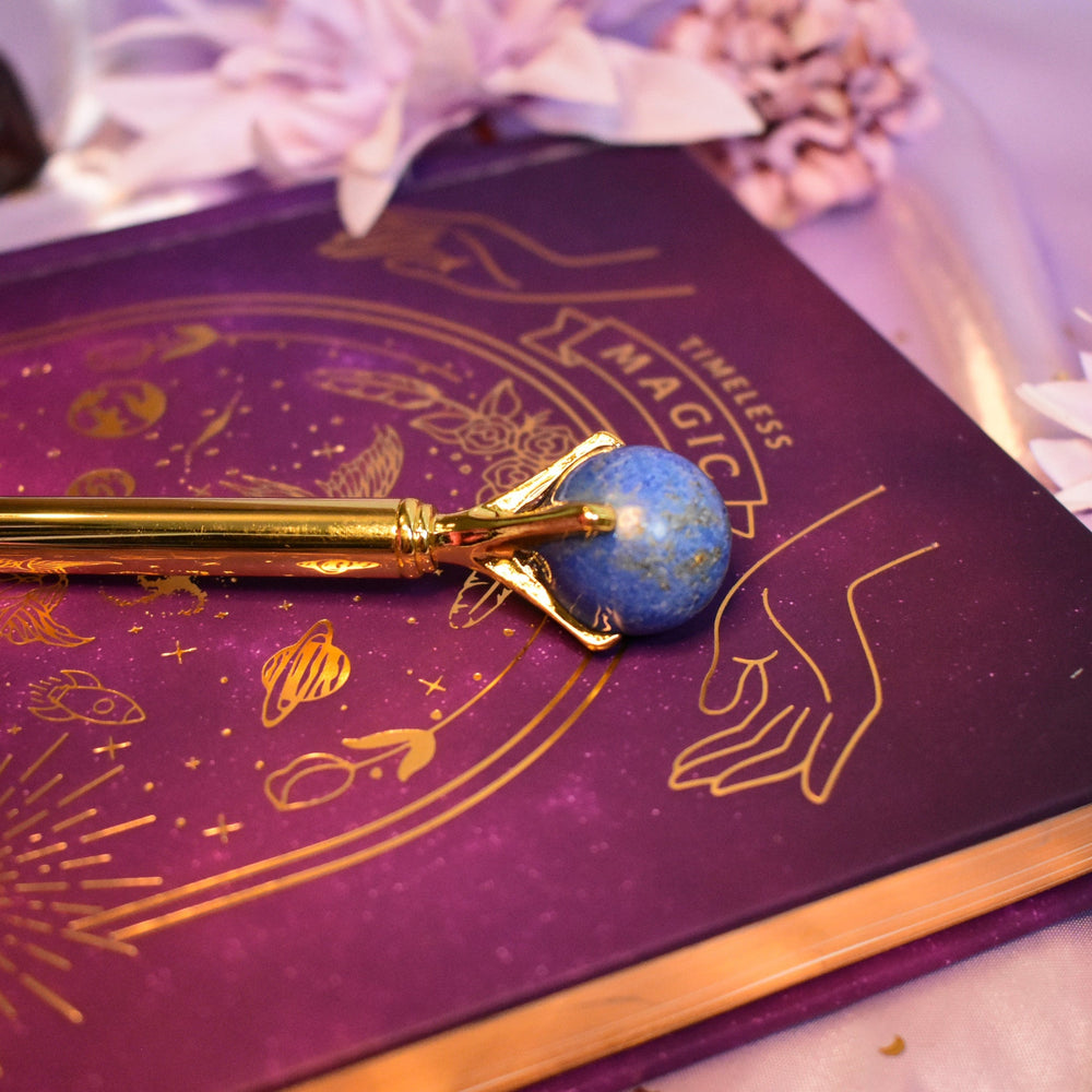 Purple book with gold designs and a blue gemstone pen on top