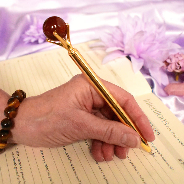 Hand holding a gold pen over a document with a purple satin background and flowers.