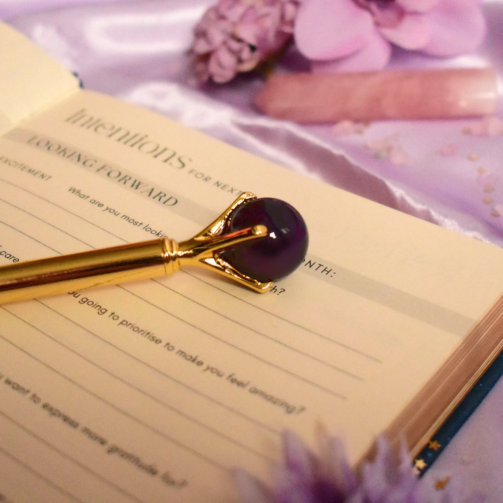Gold pen with purple accent on an open book with flowers in the background